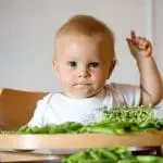 Bébé pendant son repas entouré de légumes verts